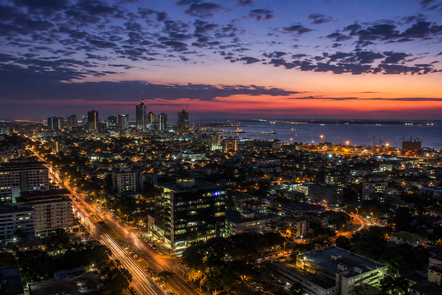 Accra at dawn, city lights still burning as the sky turns from indigo to orange over the sea.